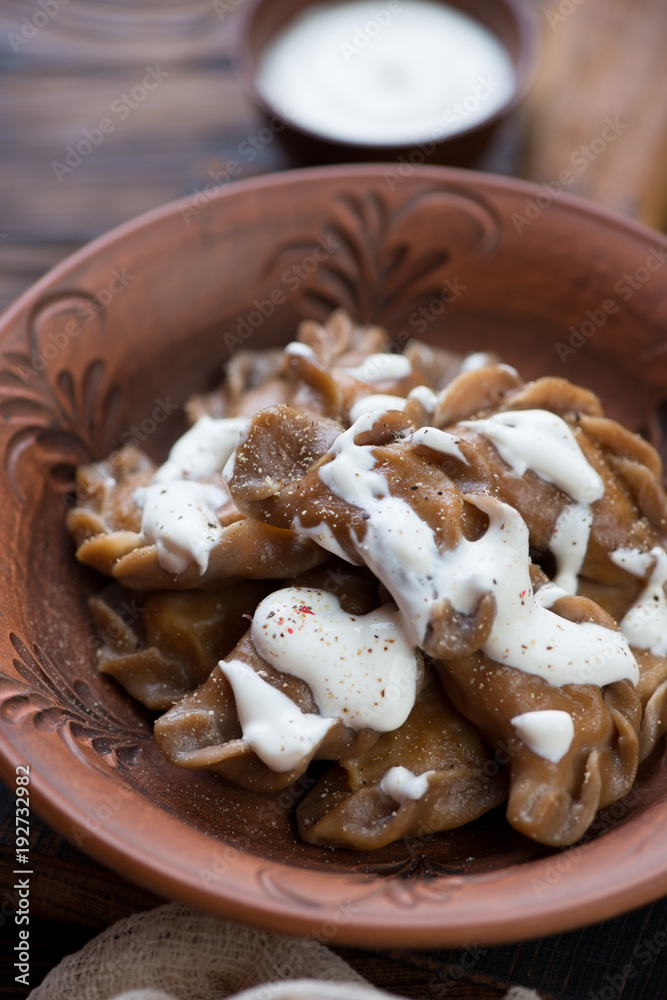 Close-up of boiled vareniki or dumplings with sauerkraut served in a clay plate and topped with sour cream, selective focus Close-up of boiled vareniki or dumplings with sauerkraut served in a clay plate and topped with sour cream, selective focus