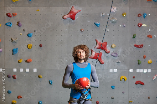 Active man in sportswear holding red protective helmet for indoor climbing