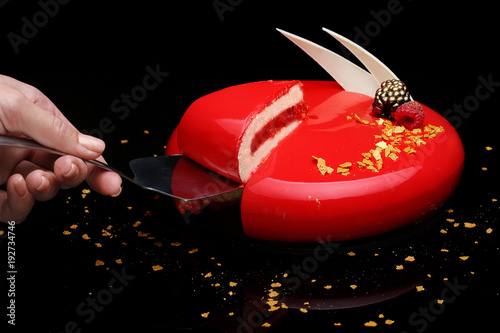 Cake with berry mousse in a mirror red glaze decorated with berries and white chocolate. The hand of the pastry chef is present in the frame. photo