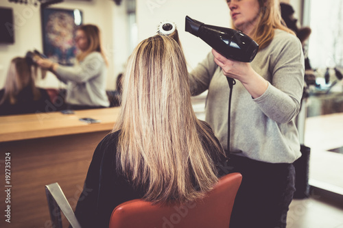 Hairstylist drying hair woman client in hairdressing beauty salon. 