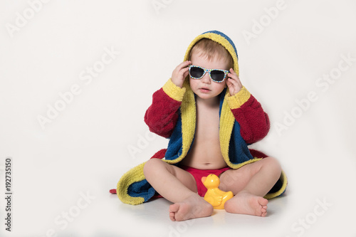 Happy child in sunglasses and bathrobe after bathing. Red, blue, yellow. The child is playing with a toy airplane. The boy is happy in his home with his parents and brothers. Hygiene and cleanliness