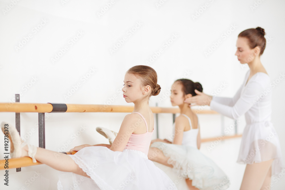 Young girls in ballet dresses keeping their left feet on bars while making stretch Young girls in ballet dresses keeping their left feet on bars while making stretch