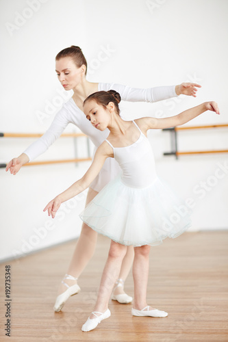 Girl and her ballet teacher stretching their arms and right legs altogether