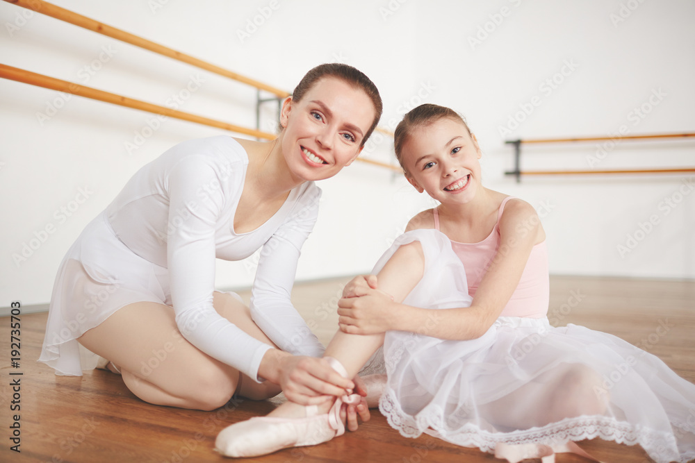 Fototapeta premium Ballet teacher helping her little learner to tie ribbons of pointe before class
