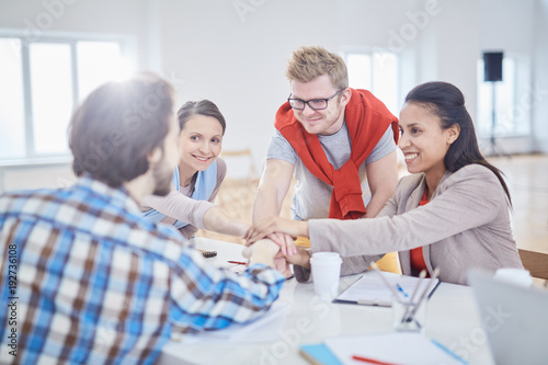 Group of happy young managers making pile of hands over workplace during meeting