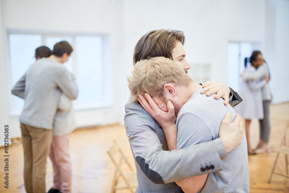 Young man supporting his crying friend in need during psychological course Young man supporting his crying friend in need during psychological course