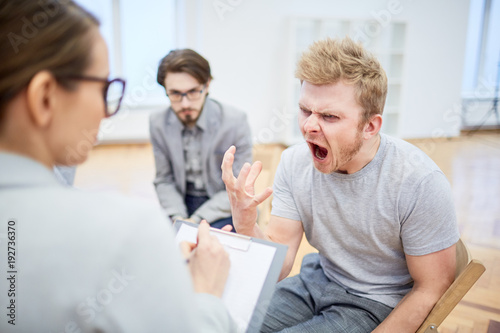 Furious young man screaming while trying to explain his problem to psychologist photo