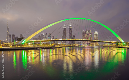 Bridge over water canal with reflection and Dubai skyline, United Arab Emirates