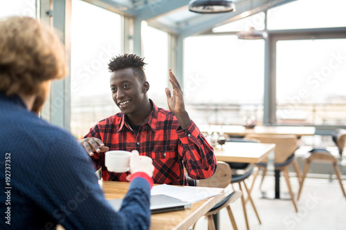 Happy young African-american man talking to his colleague or friend by cup of coffee in cafe © pressmaster