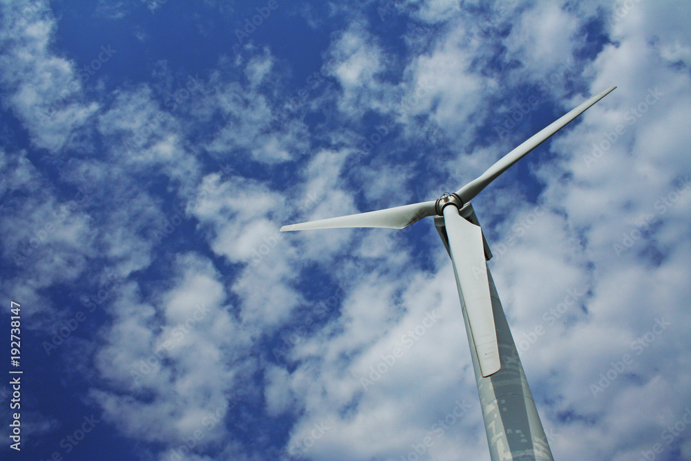 Bright picture of wind turbine headed to the cloudy blue sky on a sunny day.
