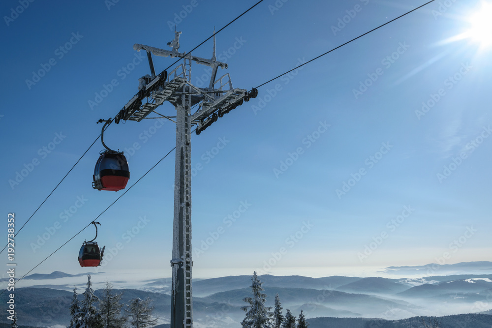 Gondola cabin lift in the ski resort over the forest on the background of snowy mountains in sunny day with copy space. Gondola cabin lift in the ski resort over the forest on the background of snowy mountains in sunny day with copy space.