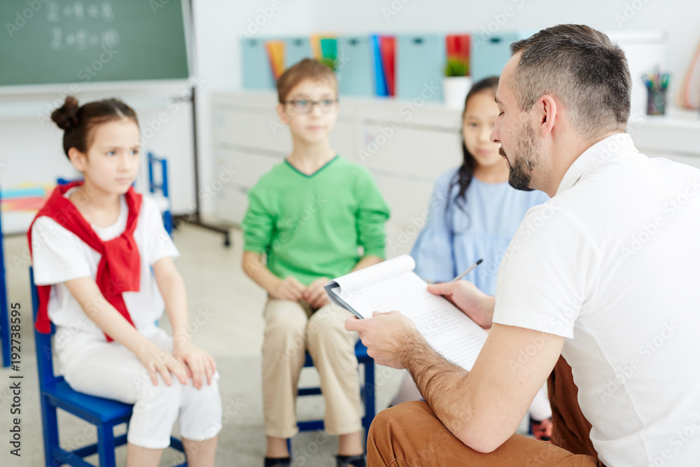 Obraz premium School psychologist reading document while siting in front of elementary students
