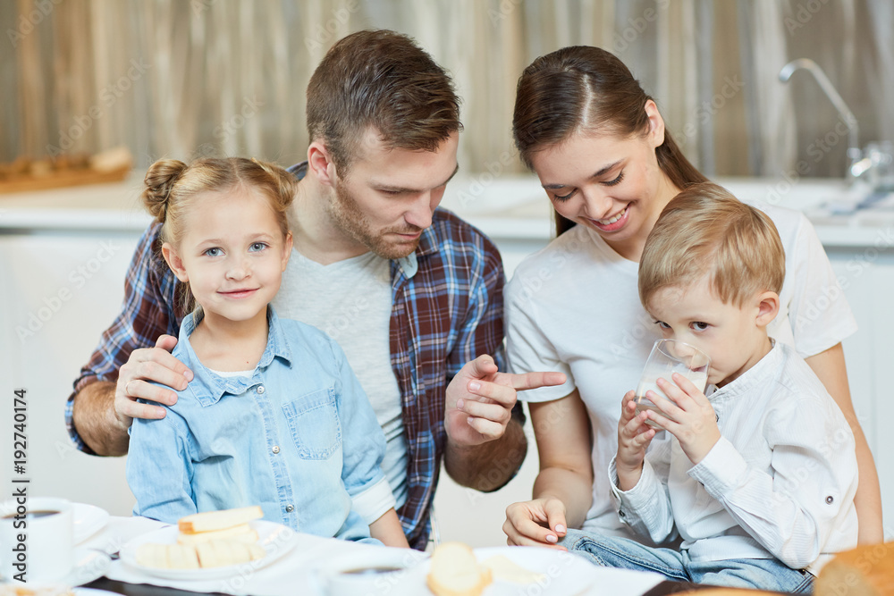 Φωτογραφία Young father pointing at glass of milk held by his little son during family brea