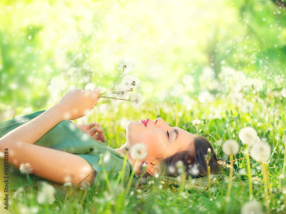 Obraz premium Piękna młoda kobieta, leżąc na zielonej trawie i dmuchanie mniszek lekarski. Koncepcja bez alergii