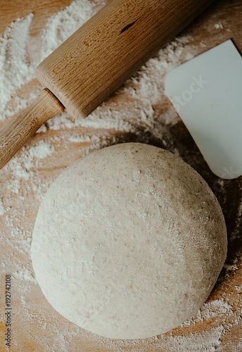 Whole wheat pizza dough shaped into ball on floured wooden background