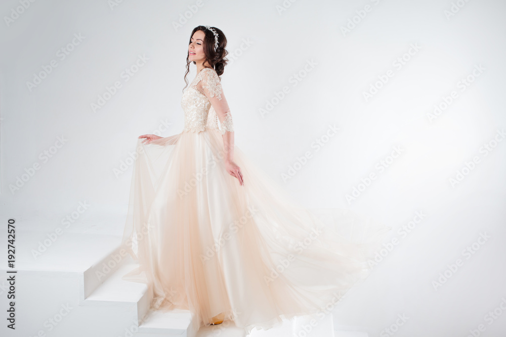 Portrait of a beautiful girl in a wedding dress. Bride in a luxurious dress standing on the stairs, climb up