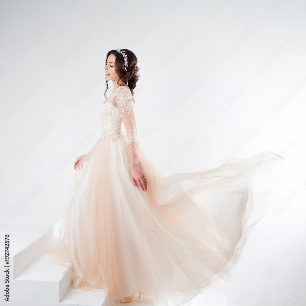 Portrait of a beautiful girl in a wedding dress. Bride in a luxurious dress standing on the stairs, climb up