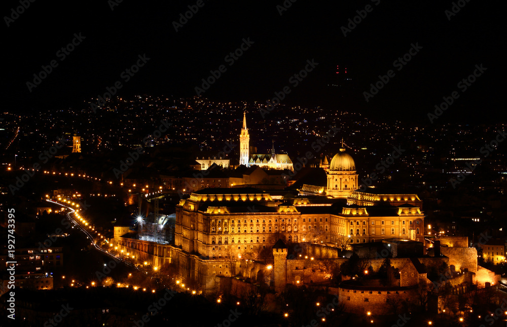 Floodlit Buda Castle Hill elevated view in evening lit by exterior lighting with Baroque Royal Palace, medieval fortifications, Matthias Church and city light dots, Budapest Hungarian capital Europe