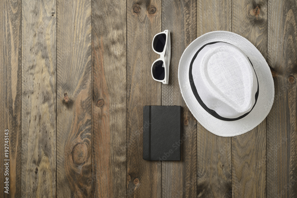 Sombrero blanco, gafas de sol y libreta sobre fondo de madera, vistos desde arriba Sombrero blanco, gafas de sol y libreta sobre fondo de madera, vistos desde arriba