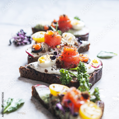 Danish open sandwich Smorrebrod with salmon on rye bread with vegetables and herbs