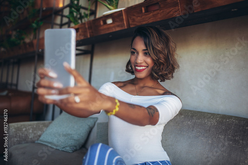 Happy black woman using digital tablets while sitting in modern cafe, make selfie photo