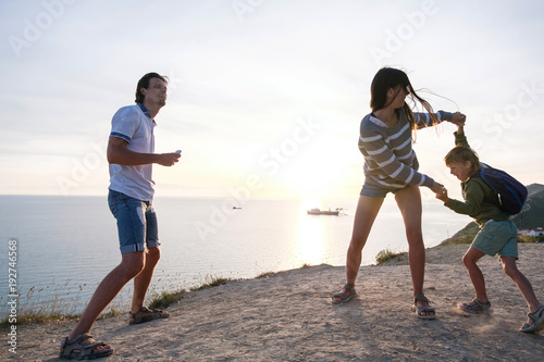 Family fun pastime on a mountain with seaside view. Dad, mom, and son dance at sunset.