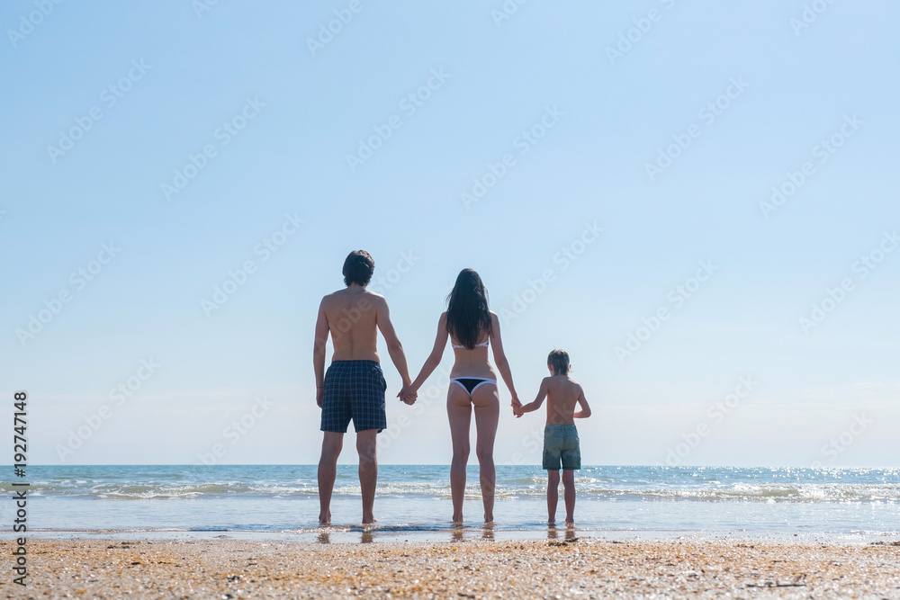 Unrecognizable family standing on the beach and looking at sea Mom son and dad hold hands back view.