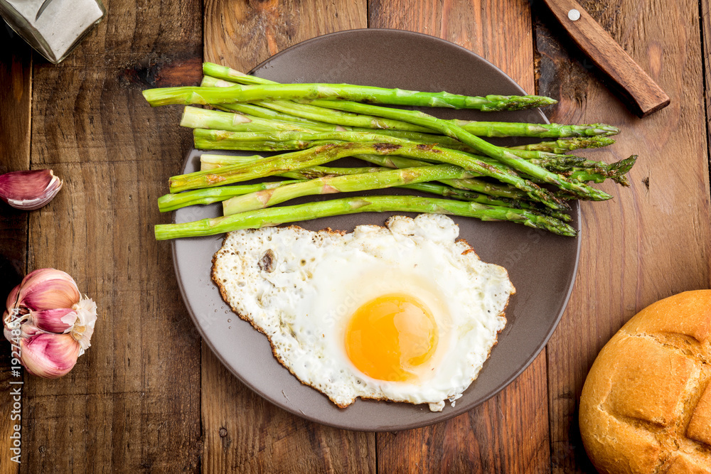aerial shot of a plate with fried egg and asparagus on barbecue on rustic wood