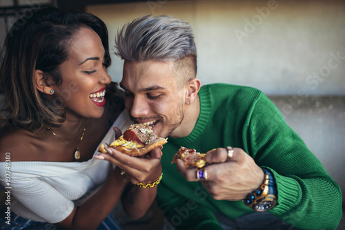 Cuadro en lienzo Mixed race couple eating pizza in modern cafe