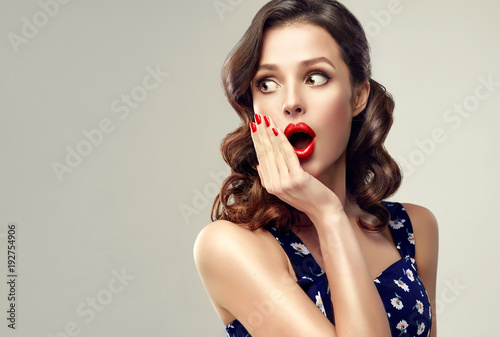 Surprised and amazed girl holds  her cheeks and looks in the side .  Beautiful woman with curly hair and red nails. Expressive facial expressions.  Presenting your product. 
