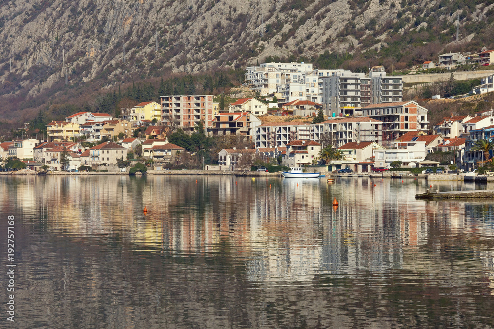 Residential area of Dobrota town, located at the foot of the mountain, is reflected in the water. Montenegro, Bay of Kotor