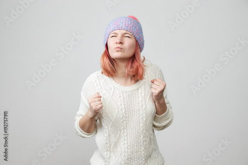 Portrait of angry stressed out young woman with clenching his lips, eyes closed and fists clenched, having mad and furious look. Aggression, negative human reaction and attitude. 