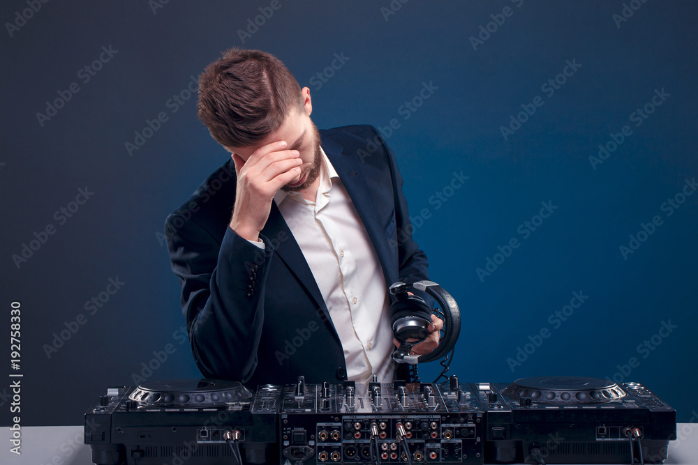 Man DJ in dark suit play music on a Dj's mixer. Studio shot. blue background. Sad of something wrong. Photo | Stock