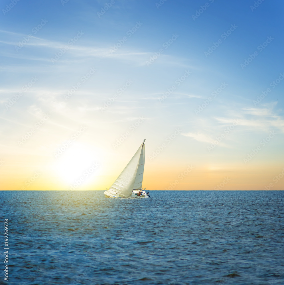 white alone sail yacht among a sea at the sunset