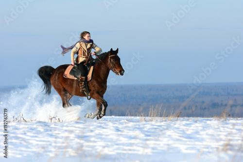 Winter horse riding on snowy field, covered dry snow with beautiful view from snowy peaks. Horseback riding with snow flying around under horse legs. Happy girl on powerful horse running gallop.