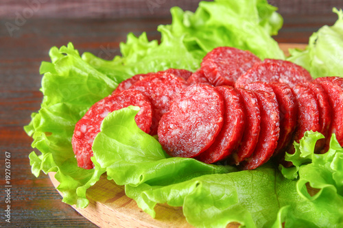 Smoked sausage, salami chopped in slices on a salad on a wooden circular cutting board on a brown table.