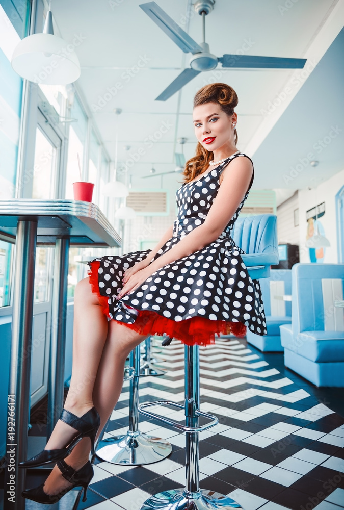 Retro (vintage) portrait of smiling cute young girl sitting in cafe. Pin up style portrait of girl dress Stock-foto | Adobe Stock