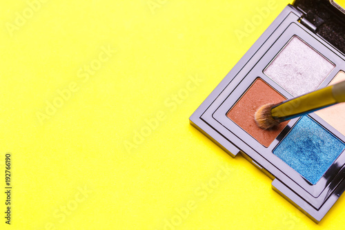 Brush for make-up over a set of eye shadow on yellow background. Copy space photo