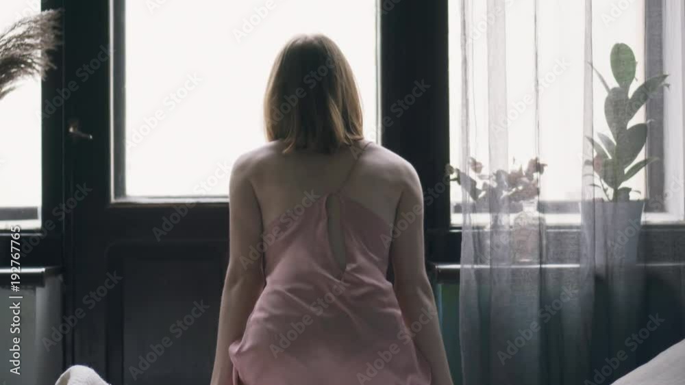 Young woman getting out of bed and looking through the window