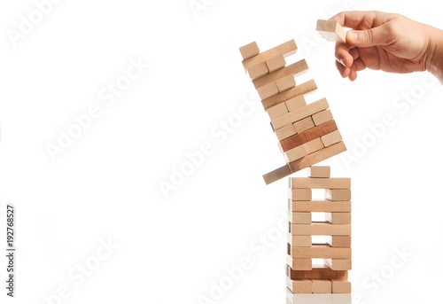 Businessman hand take one block from tower of wooden blocks and tower collapses on white background with copy space. Strategy game as a business plan for team work