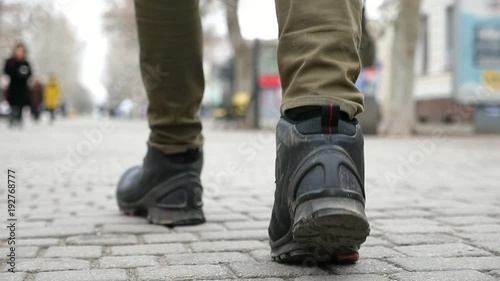 An original view of a young man`s feet walking on a tiled city street in winter in slow motion. The feet are in trendy black boots.   photo