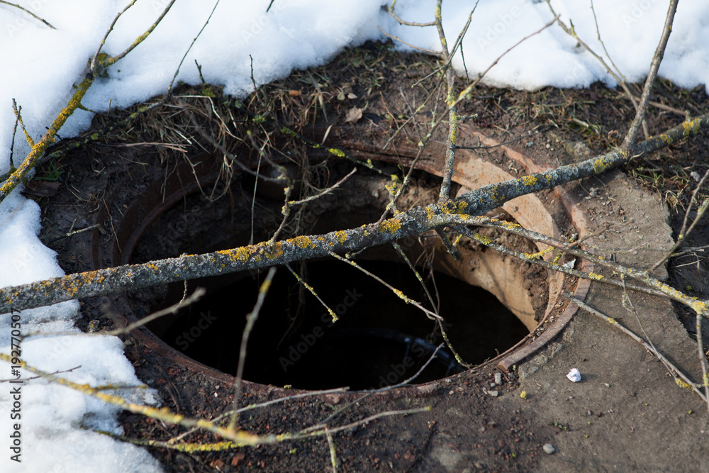 Obraz premium Dangerous manhole without a cover laid wooden planks closeup