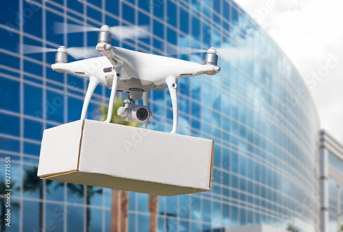 Unmanned Aircraft System (UAS) Quadcopter Drone Carrying Blank Package Near Corporate Building.