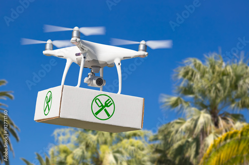 Unmanned Aircraft System (UAV) Quadcopter Drone Carrying Package With Food Symbol Label Over Tropical Terrain.