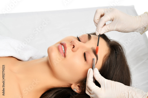 Beautician doing permanent eyebrows makeup. Closeup composition of beautiful woman face with thick brows In beauty salon