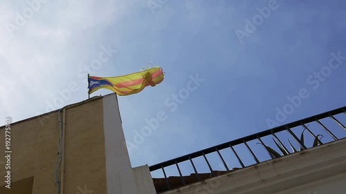 Catalonia red and yellow flag with star waves on house top under blue sky on sunny day, slow motion photo
