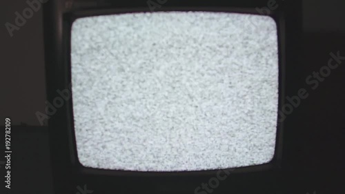 Old style black plastic TV set, camera flying into white static noise screen on floor in dark room flashing light