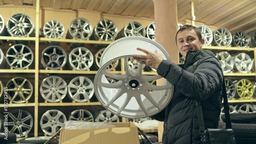 The man buys alloy wheels in his shop for his car. He takes a disc out of the box and looks at it. The white wheel is very beautiful and steep. Drawing and form of the disc are thin knitting needles photo