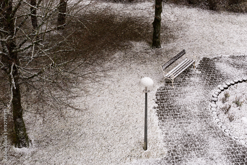 Park bench and slightly snow-covered ground from a bird's eye view Park bench and slightly snow-covered ground from a bird's eye view
