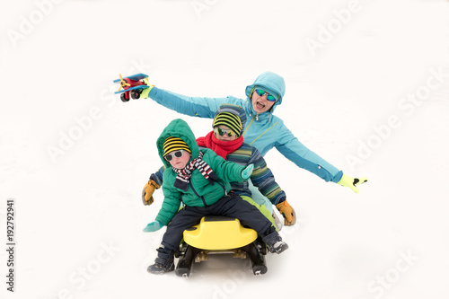 Young girl in a blue ski suit plays in the snow with her children. Yellow sledges, sunglasses, bright clothes. Children are happy together. The concept of a funny winter vacation for the whole family